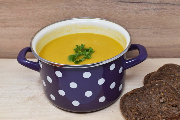 Vaisselle Emaillée purple enamel pot with white polka dots, 2L capacity, filled with yellow soup and garnished with parsley.